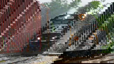 A photograph of a locomotive pulling boxcars. Some parked boxcars are next to the locomotive.
