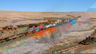 A photograph of a train pulling intermodal containers across a field.