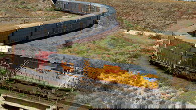 A photograph of a locomotive hauling a line of railcars in a grassy field.