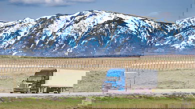 unidentified tractor-trailer on highway with snowy mountains in backdrop