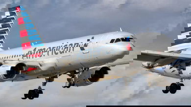 Silver plane comes in for landing with wheels down.
