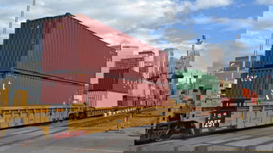 A photograph a train carrying intermodal containers. Tall city buildings are in the background.