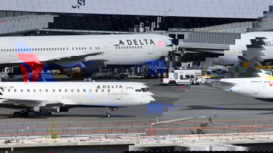 A big white Delta jet next to a smaller one at airport.