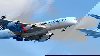 A white super-jumbo jet on approach to land in blue skies.