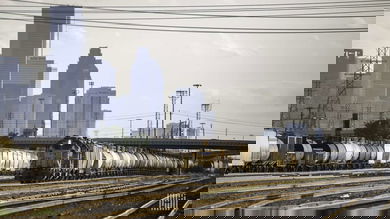 A photograph of a train at a rail yard. There are tall buildings and skyscrapers behind it.
