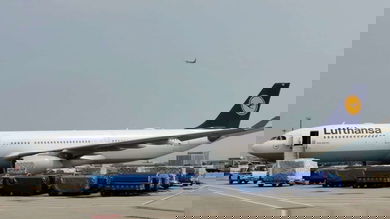 A big white jet with blue tail surrounded by cargo carts on the ground.