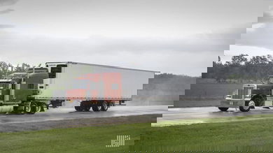 Tractor-trailer on wet highway with storm cloud in the background.