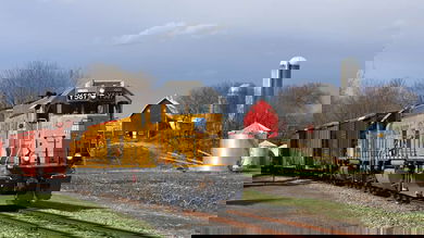 A photograph of a train traveling past a farm.