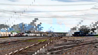 A photograph of a rail yard with train tracks and a train. There is a city with skyscrapers far in the distance behind the train.