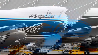A blue-and-white 747 jumbo cargo jet parked at airport.
