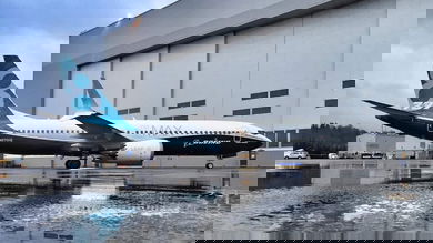 A blue and white 737 MAX next to a hangar at a Boeing facility.