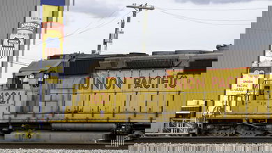 A photograph of a train locomotive by a buidling.