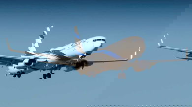 A white jet approaching for landing with wheels down.
