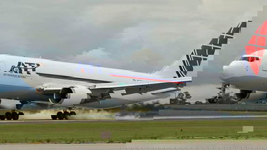 A big white jet touches down on the runway, with smoke coming from wheels.