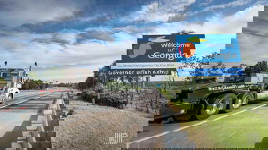 A flatbed commercial truck passes a sign that reads "Welcome to Gerogia"
