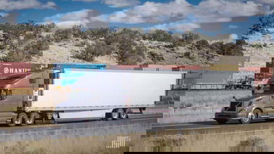 A photograph of a truck with a trailer and an intermodal train behind the truck.