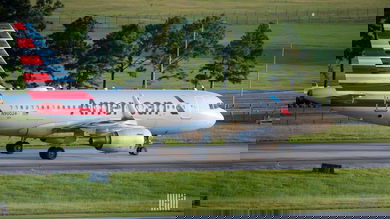 A silver American Airlines plane with red, white and blue striped tail rolls down taxiway. American plans to cut 19,000 jobs.