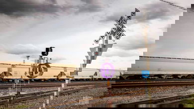 A photograph of a train hauling grain hopper cars. The train is at a railroad crossing.