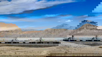 A photograph of a train with hoppers. The train is crossing a desert-like landscape.