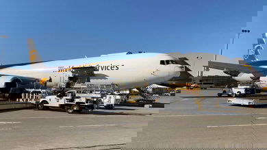 A white UPS plane with brown tail sits on ramp with cargo door open on side.