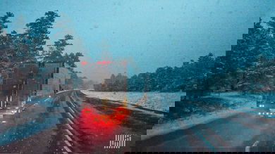 Tractor-trailer heading down slick highway with snow in the surrounding hills nd mountains.