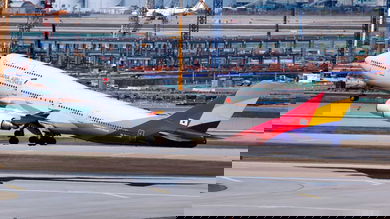 An Asiana jumbo jet with white fuselage and multicolored tail lifts off from runway.