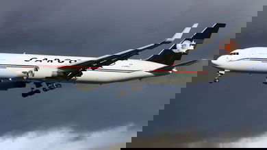 A white jet with a blue tail and the name Cargojet on its side has wheels down as it flies low to start landing.