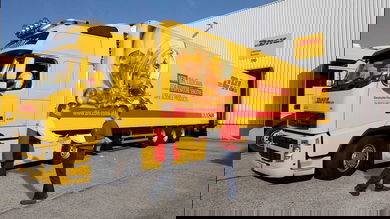 A bright yellow refrigerated DHL truck backed up to loading dock.