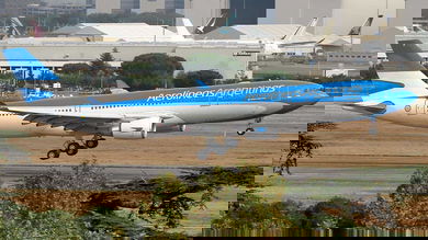 A blue-and-white jet comes in for landing with wheels down.