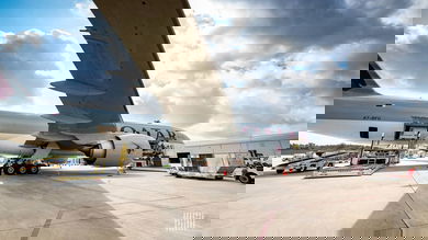 A big cargo plane with door open to load cargo. Photo from side, under wing on a sunny day.
