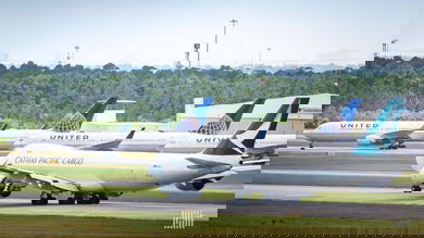 A white jumbo jet begins to move down runway with parked planes in the background.