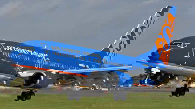 A bright blue Boeing 737 with orange lettering lands on runway.