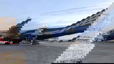 A cargo pallet sitting on tarmac next to a big white and blue jumbo jet.