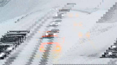 Cars and tractor-trailers behind a plow truck on a snowy Michigan highway.