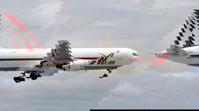 A large white plane with wheels down comes in for a landing.