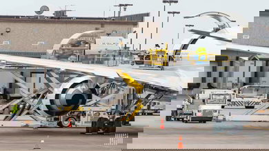 Wing of a plane viewed from behind the plane, with cargo being loaded in side door.