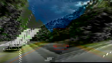 Tractor-trailer heading down a highway with lightning across the sky.