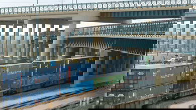 A photograph of a train with intermodal containers traveling underneath a bridge.