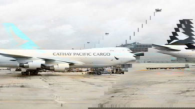 A white 747 jumbo jet with a green tail operated by Cathay Pacific Cargo sits on a wet tarmac.