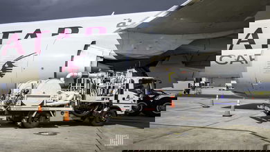 A gray Qatar Airways jet being refueled by a truck.