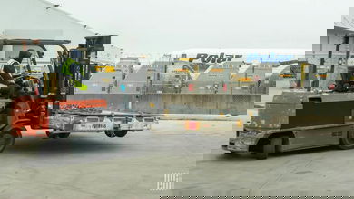 A forklift driver with a pallet, airfreight containers in a row and an aircraft in the background.