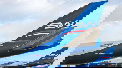 Back end of a white jet, with a blue tail and initials SW on it.