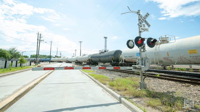 A photograph of a train of tank cars at a rail crossing.