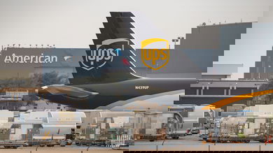 A UPS plane's tail at an airport with air cargo below to illustrate an article about cybersecurity reporting requirements for the rail and air sectors.