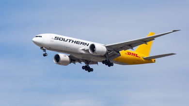 A Southern Air jet with a white front and mustard colored back section comes in for a landing with wheels down against blue sky.