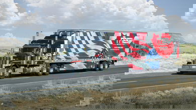 A semi-truck with a Canadian and US flag on the trailer travels on a higheway.
