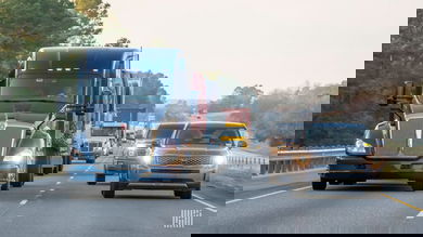 A line of trucks traveling at the same speed as passenger vehicles in the left lane