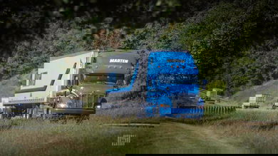 A blue and white commercial truck with the logo of Marten Transport traveling on a road