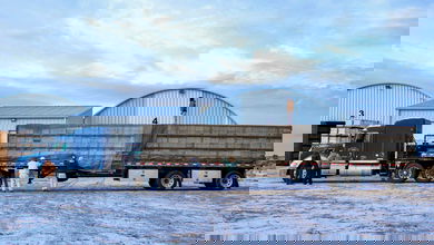 A blue tractor trailer is being loaded up with honeybee hives secured by netting and straps.