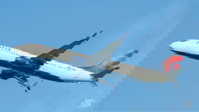 A blue, red and white Delta Air Lines plane in the sky, view from below.